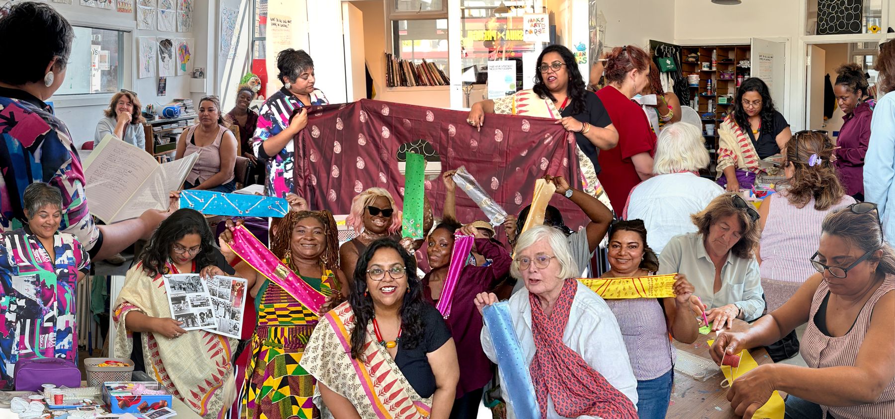 A full room of participants holding up sarees and mini sarees at a Saree Stories workshop